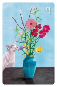 9 Die Blumen im Magic Cat Lenormand. Es ist eine weiße Katze zu sehen, die an einem Blumenstrauß riecht.